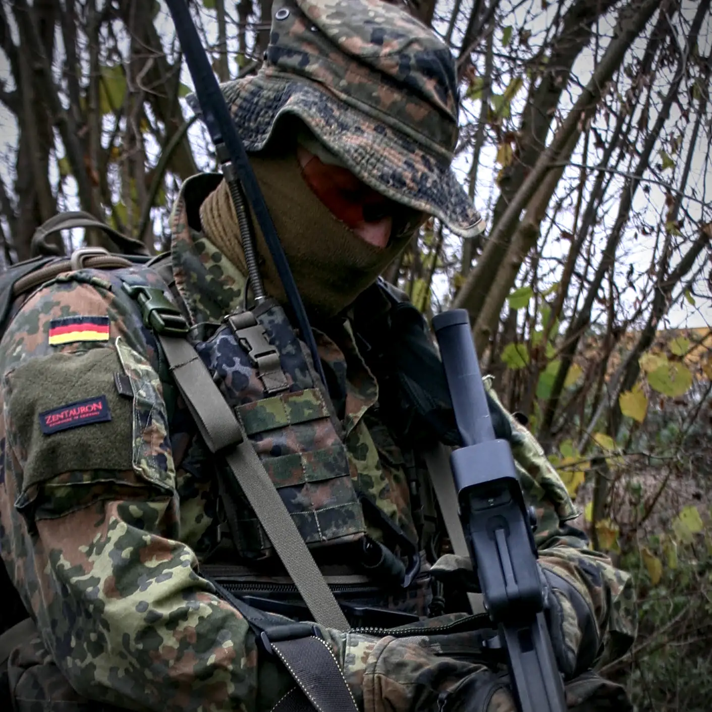 Anwendungsbeispiel der Funkgerätetasche SEM 52 Soldat in Flecktarn-Ausrüstung mit Funkgerät und Funkgerätetasche SEM 52 im bewaldeten Gelände.