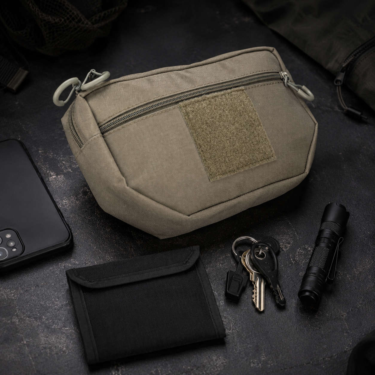 Vorderansicht  der Hüfttasche EDC in der Farbe Steingrau-oliv mit Smartphone, schwarzer Geldbörse, Schlüsselbund und Taschenlampe auf dunkler Oberfläche.