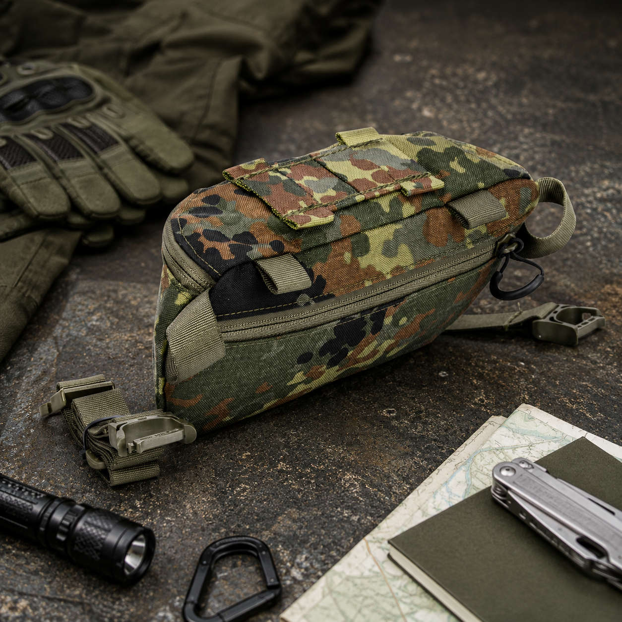 Rückansicht der Hüfttasche Modular in der Farbe Flecktarn, umgeben von Handschuhen, Taschenlampe, Karabiner, Karte, Notizbuch und Multitool.