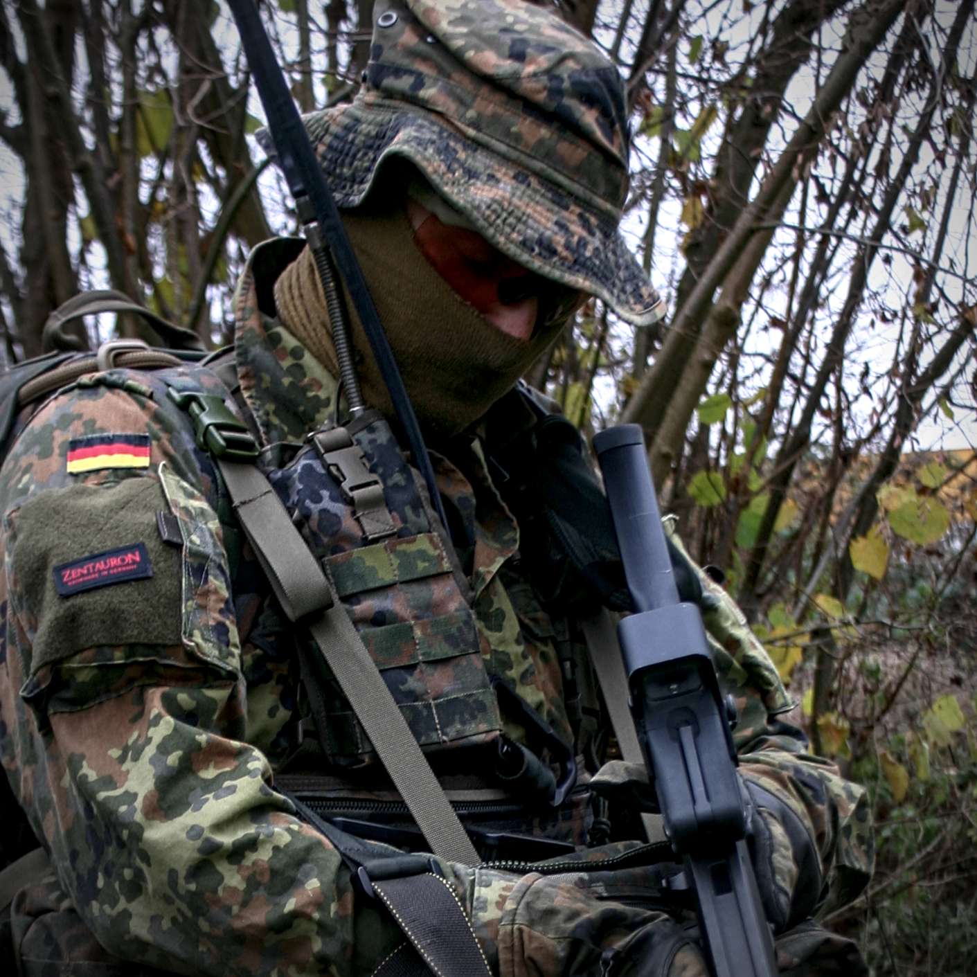 Anwendungsbeispiel der Funkgerätetasche SEM 52 Soldat in Flecktarn-Ausrüstung mit Funkgerät und Funkgerätetasche SEM 52 im bewaldeten Gelände.