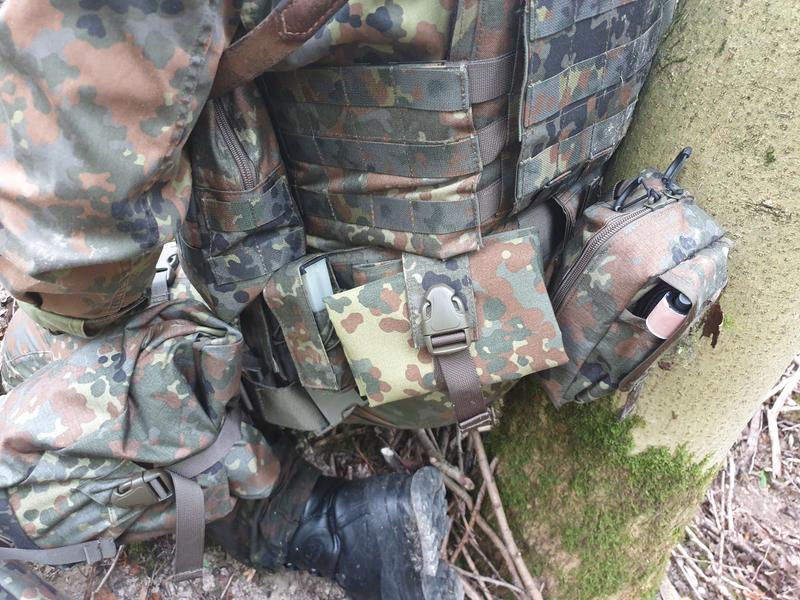 A soldier kneels next to a tree, the drop bag is attached to his equipment with MOLLE loops.